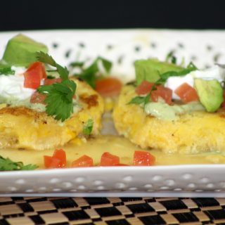 two tamale cakes sitting on a white plate topped with pico, sour cream, and avocado chunks